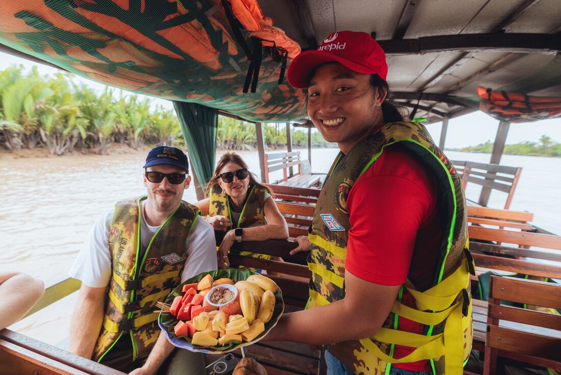 Intrepid Leader serving fruit to Travellers on a boat on the Mekong Delta, Vietnam