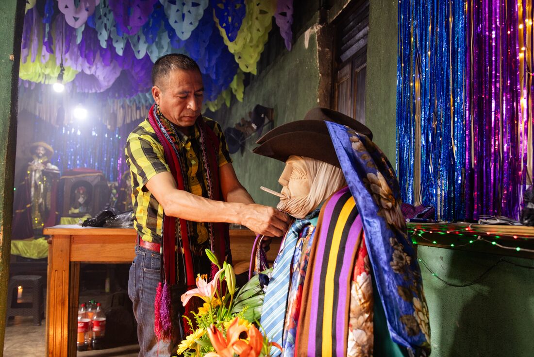 Guatemalan local affixes fabric to a statue of San Simon in an Atitlan home smoking ceremony