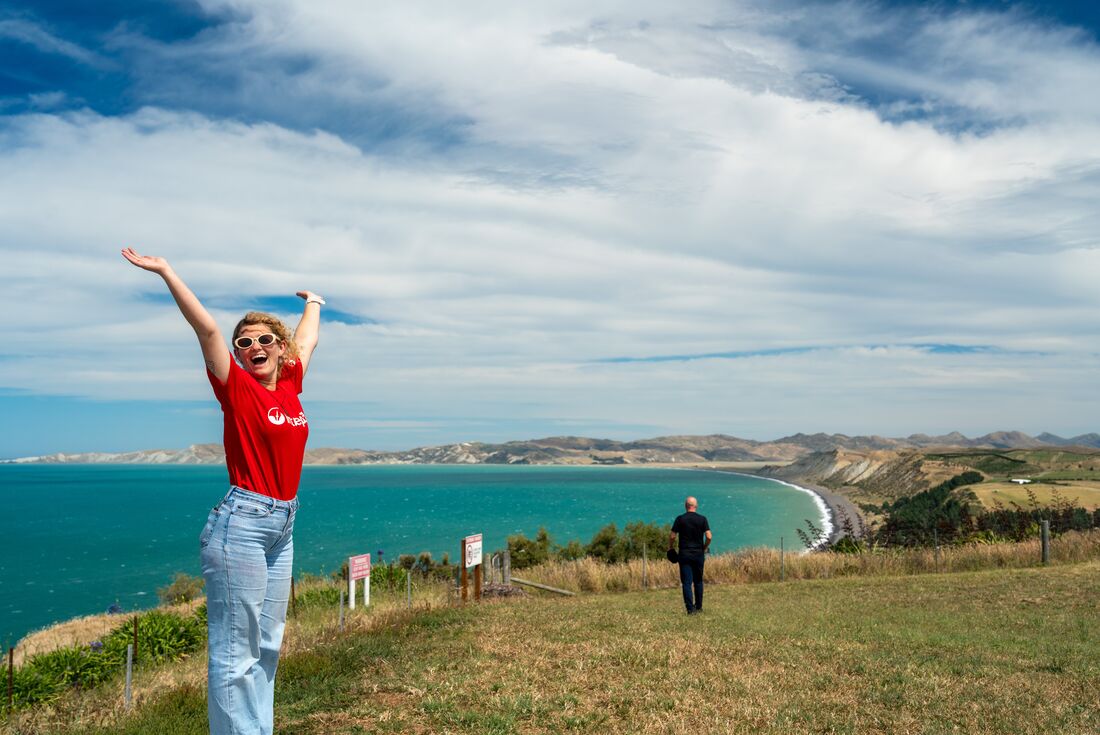 Leader throwing her hands up with a scenic coastal view behind her at Marlborough Sounds, New Zealand