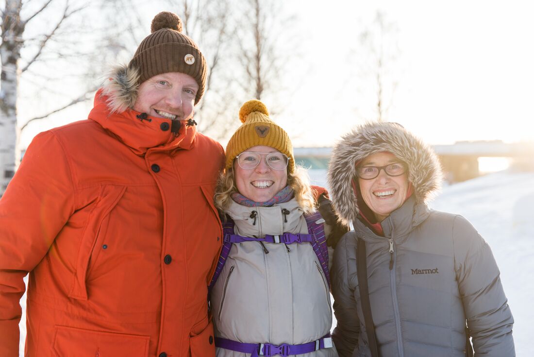Leader and travellers in heavy winter coats smile in the snowy city of Rovaniemi