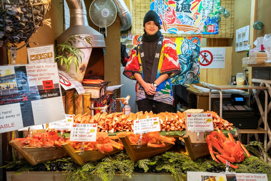 Local vendor at Nishiki market stall with crab and seafood for sale in Kyoto Japan