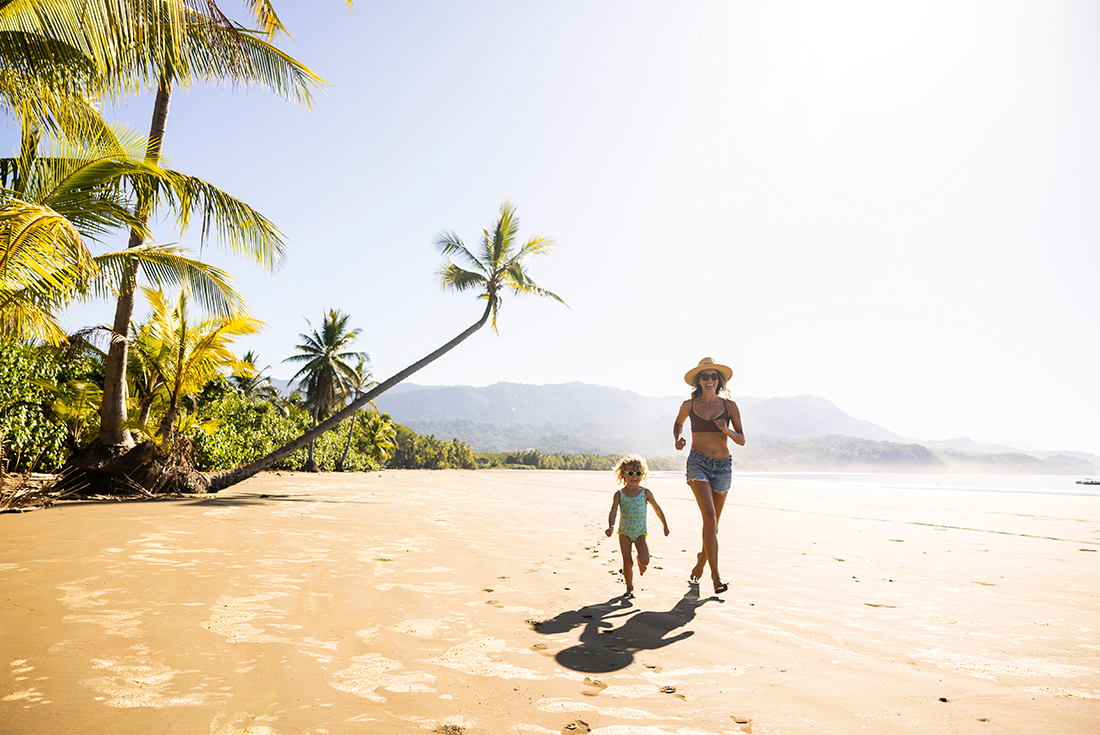 Mother and daughter run along the palm scattered Dominical Beach, Costa Rica