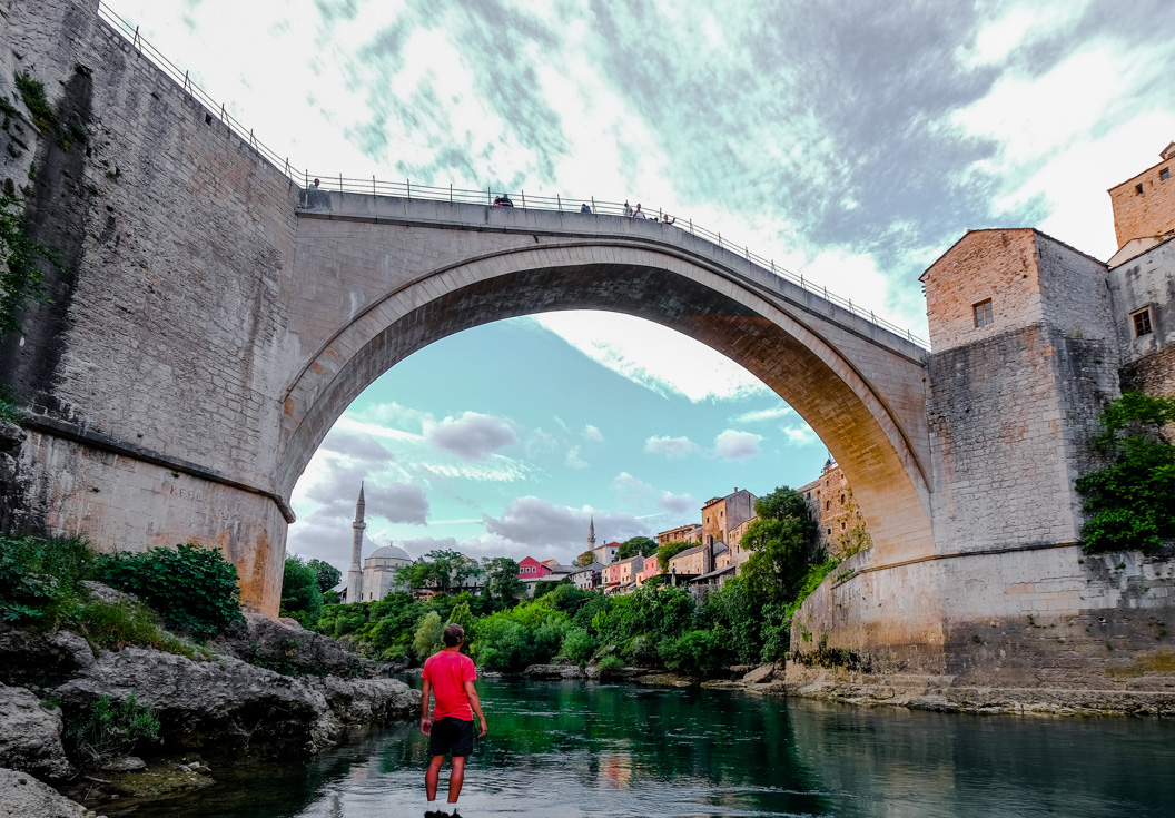 Intrepid traveller looks up from riverbed at the majesty of an ancient Ottoman bridge in Mostar Bosnia and Herzegovina