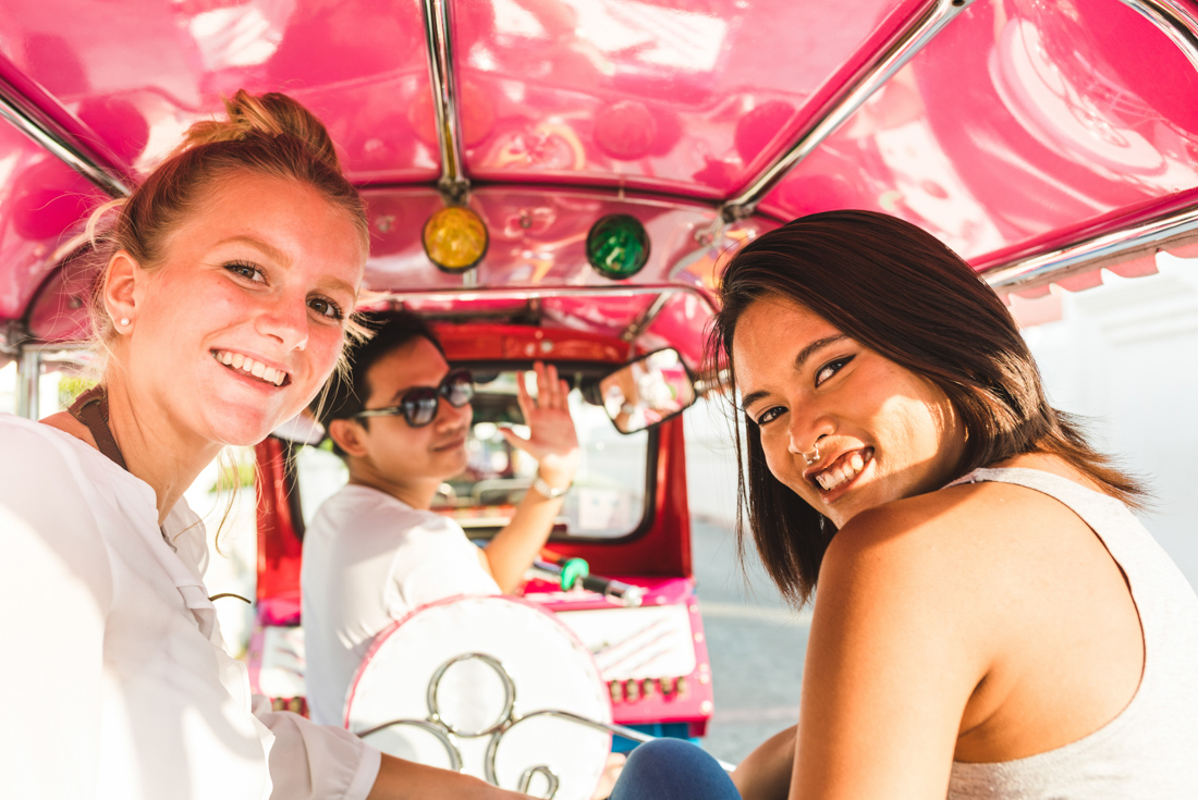 Friends smile at camera enjoying a tuk tuk ride in downtown Bangkok in Thailand 