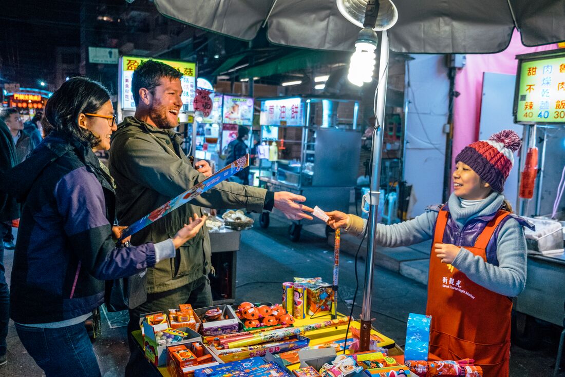 Two travellers talk happily with shop owner as they buy gifts in Taipei night markets