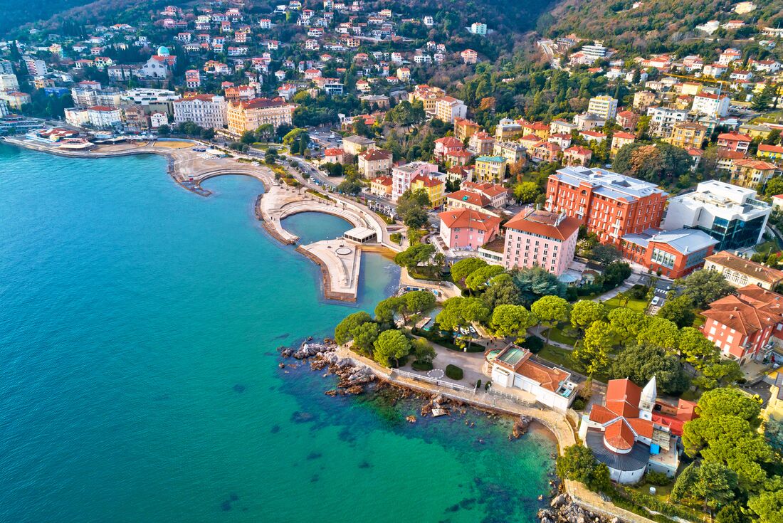 An aerial drone view of the coastal town Opatija in Croatia, showing rooftops and treetops 