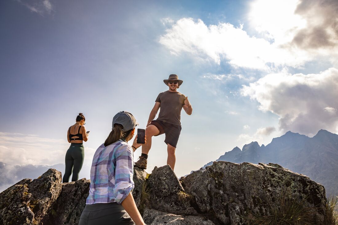 Traveller smiles down and makes a thumbs up looking down from a rocky peak at the second pass of the inca Trail