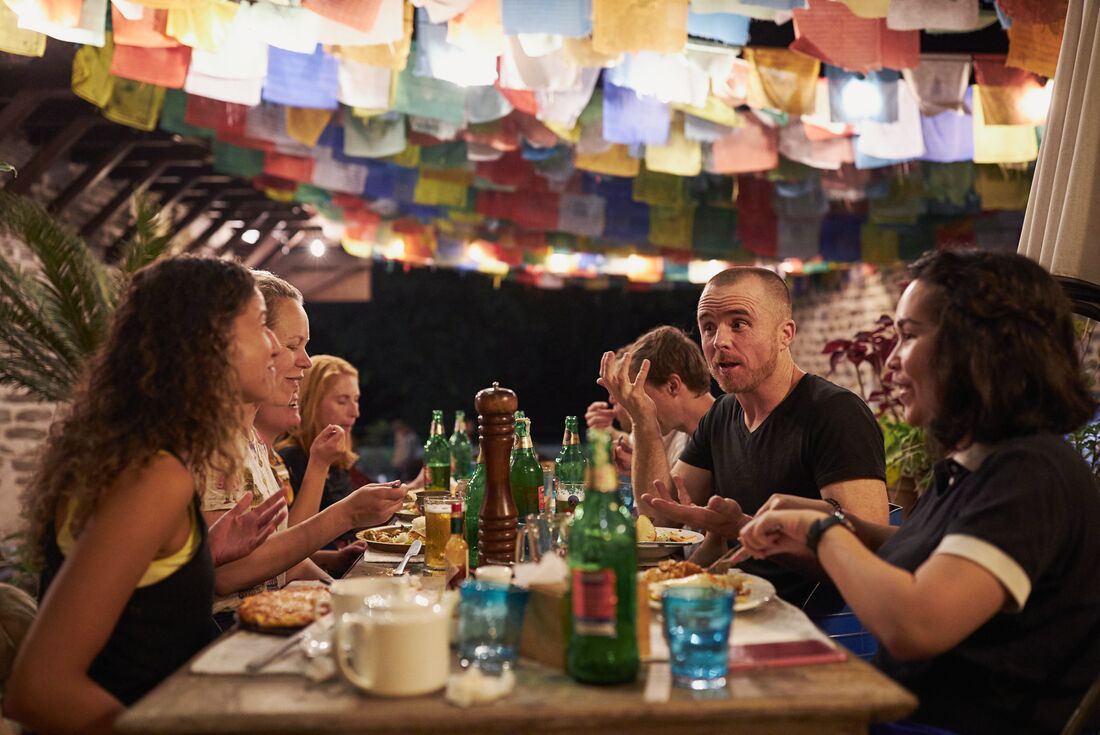 Travellers talk smile and laugh over dinner in Pokhara with prayer flags overhead in Nepal
