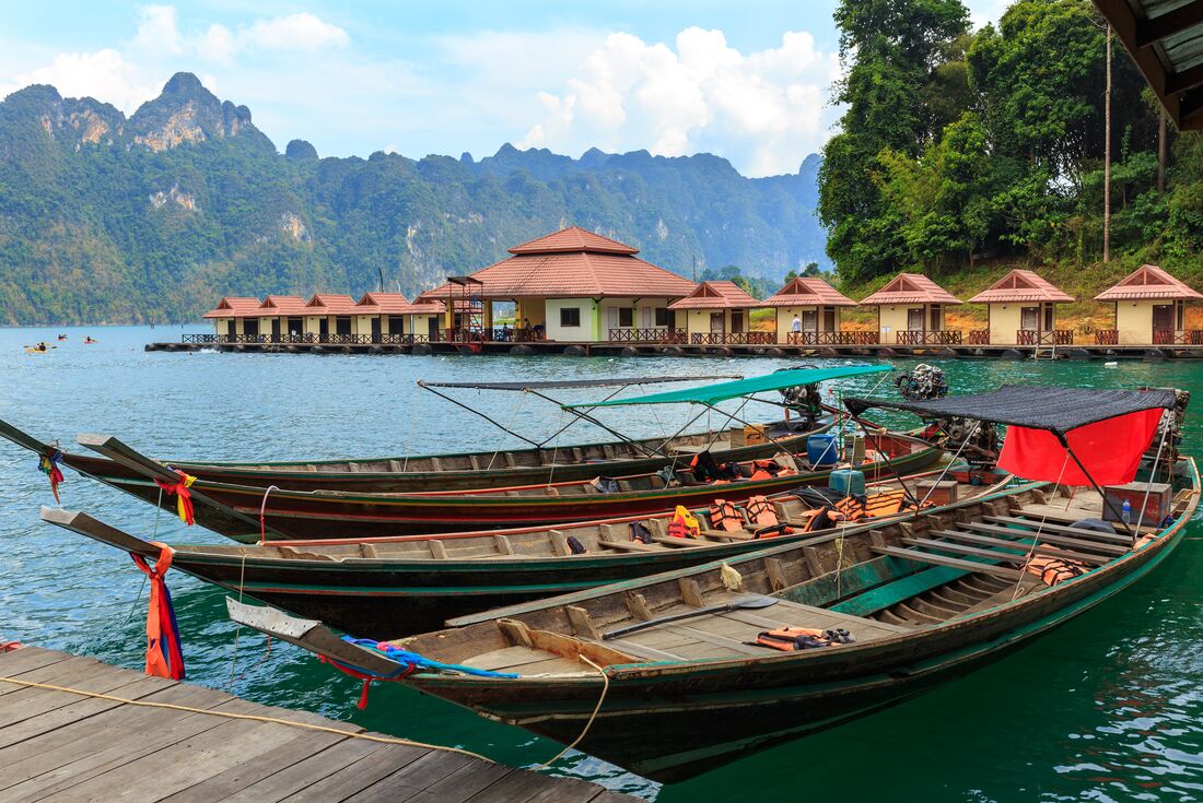 Longtail boats docked at Cheow Lan Lake rafthouse with huge limestone mountains in the ocean in background