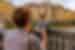 Leader takes a photo of traveller standing on a bridge in Florence with yellow buildings in the background, Italy