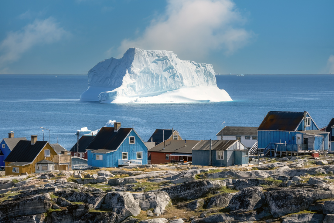 Qeqertarsuaq town colourful wooden buildings with enormous iceberg visible beyond the town