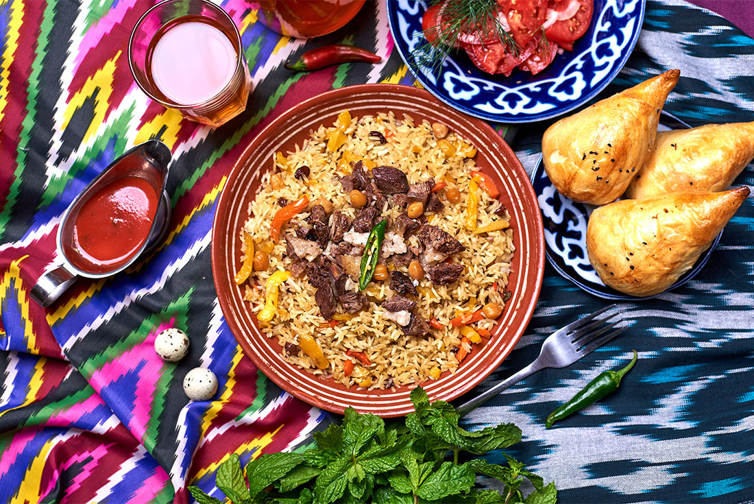 Traditional Uzbekistani plov with samsa, juice, chili and salad