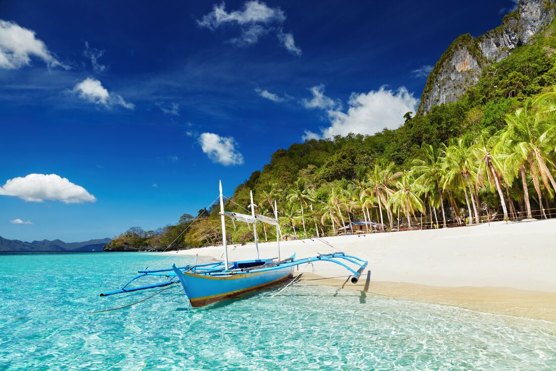 A beach of the El Nido island with a traditional pontoon boat