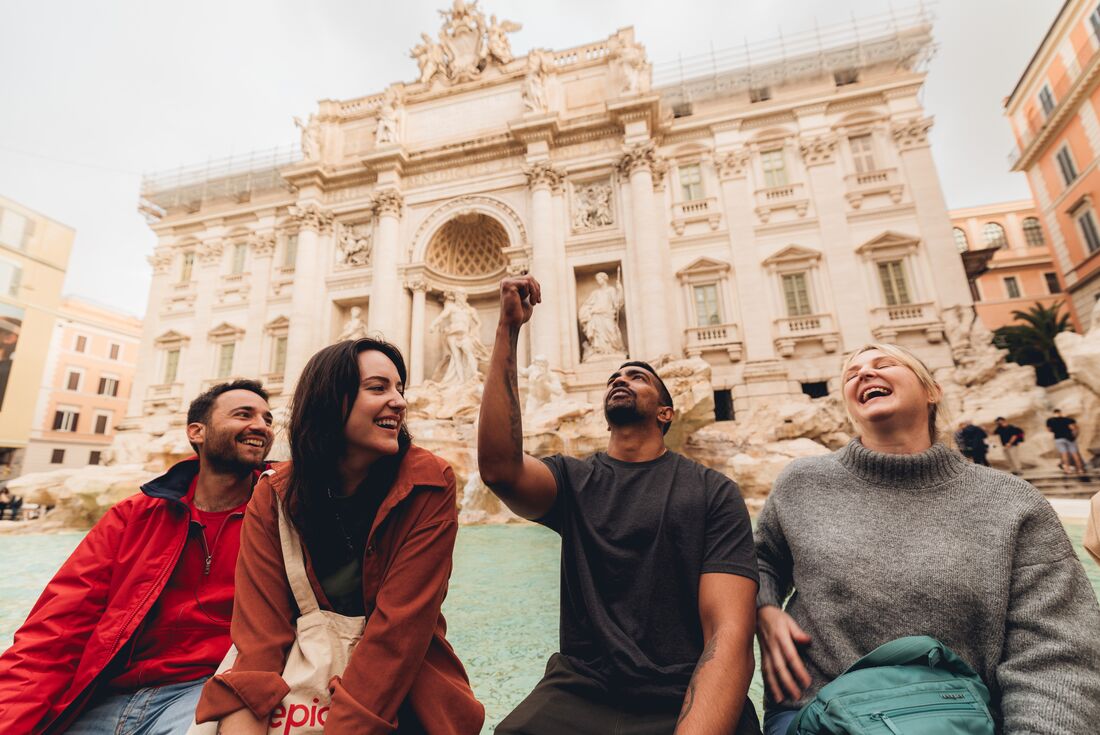 Travellers smiling as one flicks coin into the Trevi Fountain, Rome, Italy