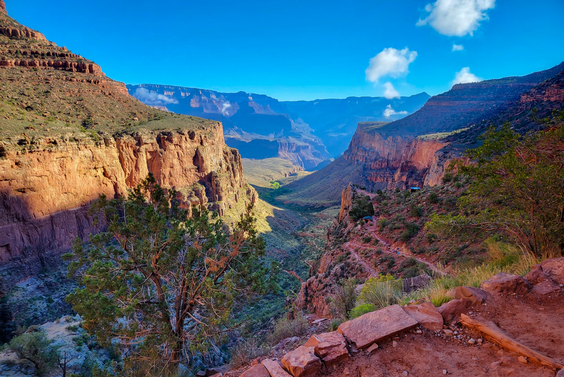 Wide view of a dip in the Grand Canyon with tiny travellers distant on a path below