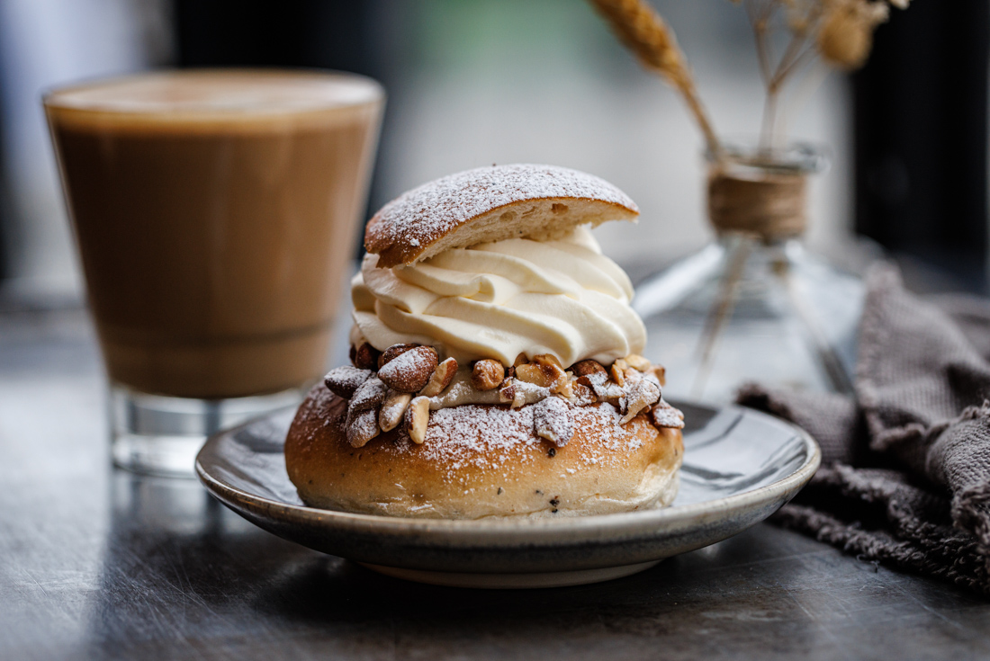 An appetizing Semla bun with almonds and heavy cream, flour and sugar and a hot latte behind