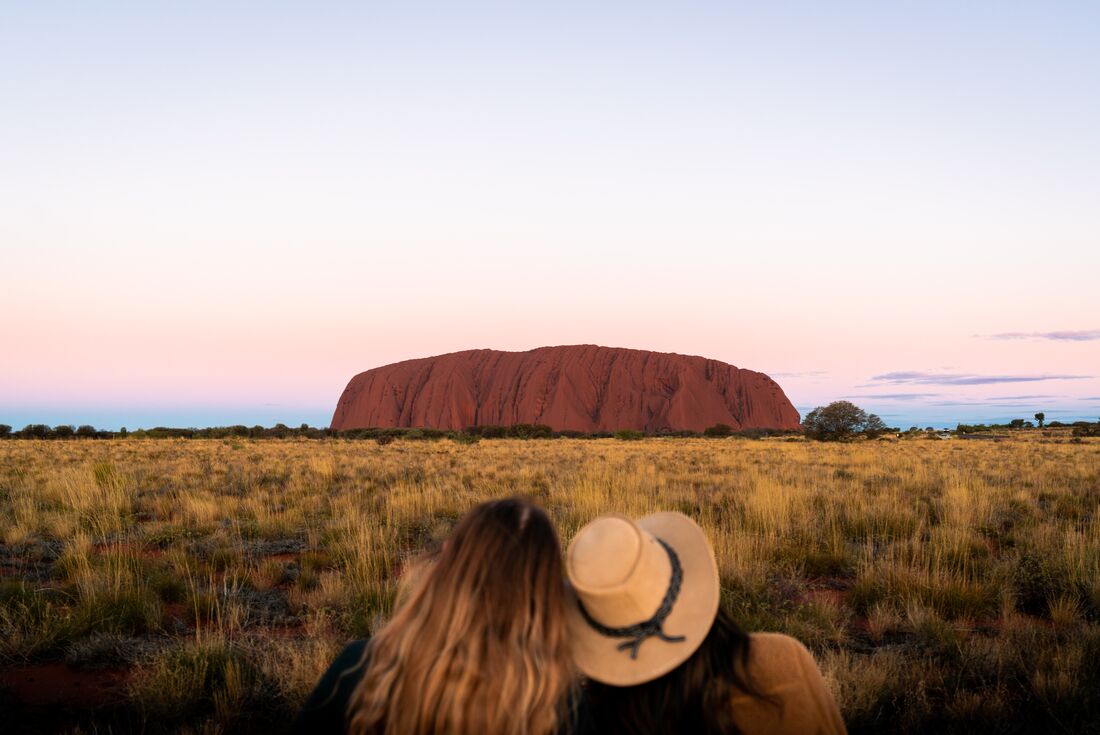 Two Intrepid travellers lean on each other looking out at Uluru in Australia's Red Centre