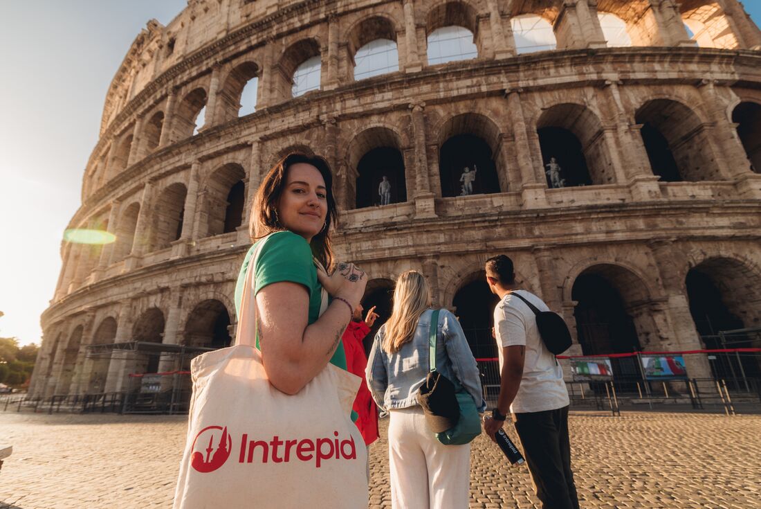 Traveller looks over at the camera as she walks towards the Colosseum at dawn, with daylight breaking through in the background, Rome, Italy