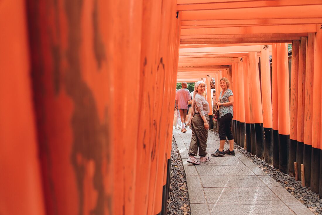 Travellers look back at viewer from the endless rows of Fushimi Inari orange shrine gates near Kyoto Japan