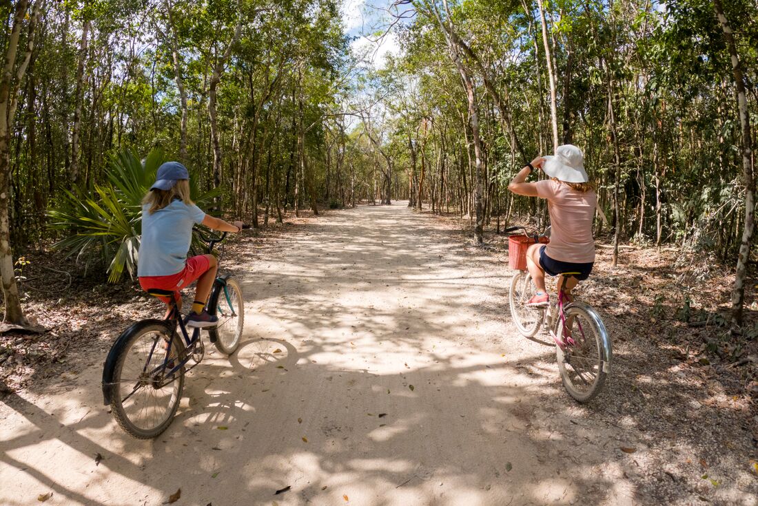 Travellers cycling on dirt path surrounded by trees in Mayan City, Coba, Mexico