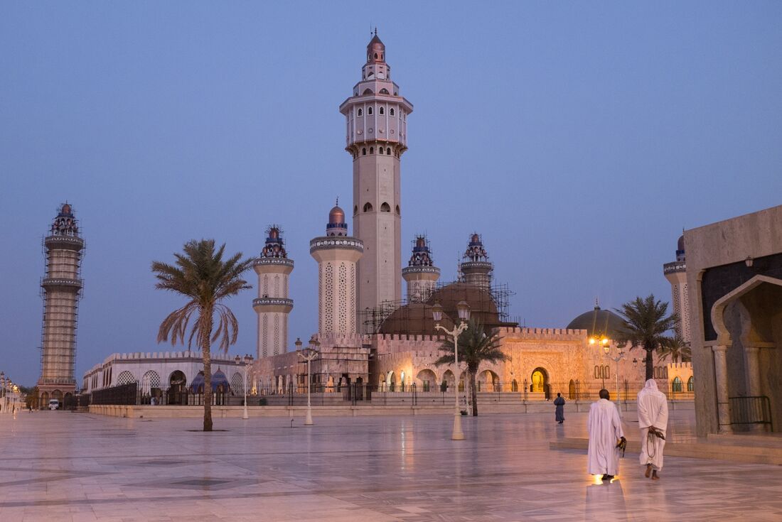 Towering spires of the Great Mosque of Touba at dawn in northern Senegal with locals in foreground