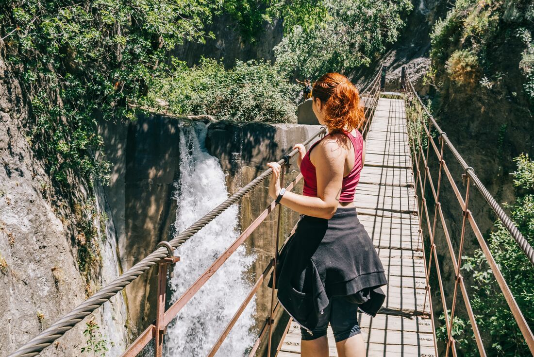 Waterfall on the Los Cahorros hike seen from suspension bridge with hiker in foreground in Sierra Nevada