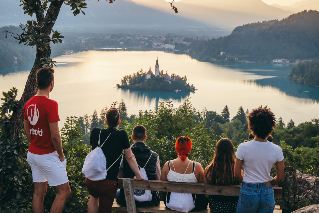 Group of travellers and leader look out over reflective Lake Bled from Ostrica mountain in Slovenia