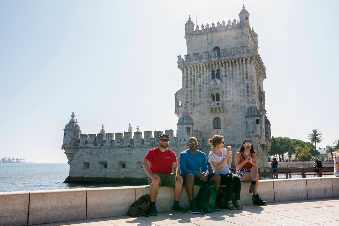 Travellers and leader sit outside the Belem tower on the waterfront of Portugal