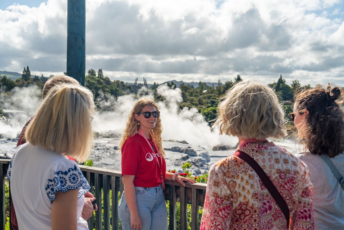 Smiling leader talking to travellers while standing in front of Pohutu Geyser, Rotorua, New Zealand