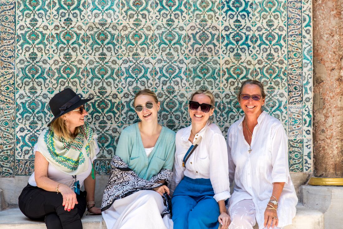 Group stop in the shade talk and laugh in front of a mosaic at Tokpapi Palace