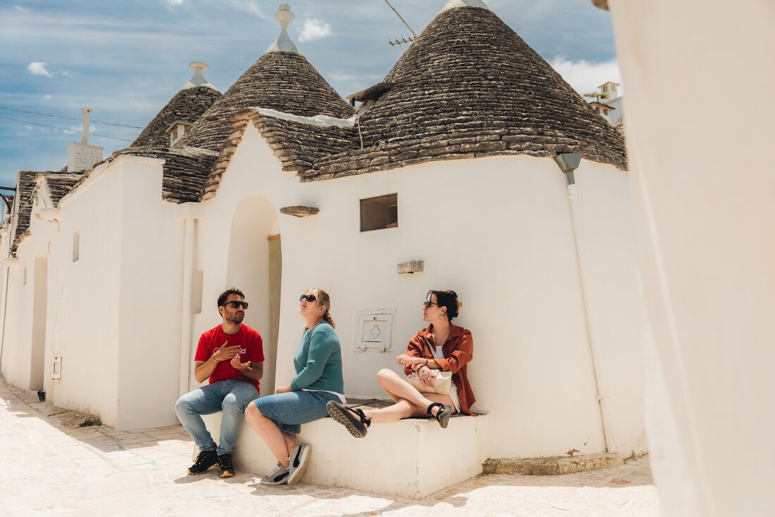 Travellers sitting on ledge outside traditional trulli buildings in Alberobello, Italy