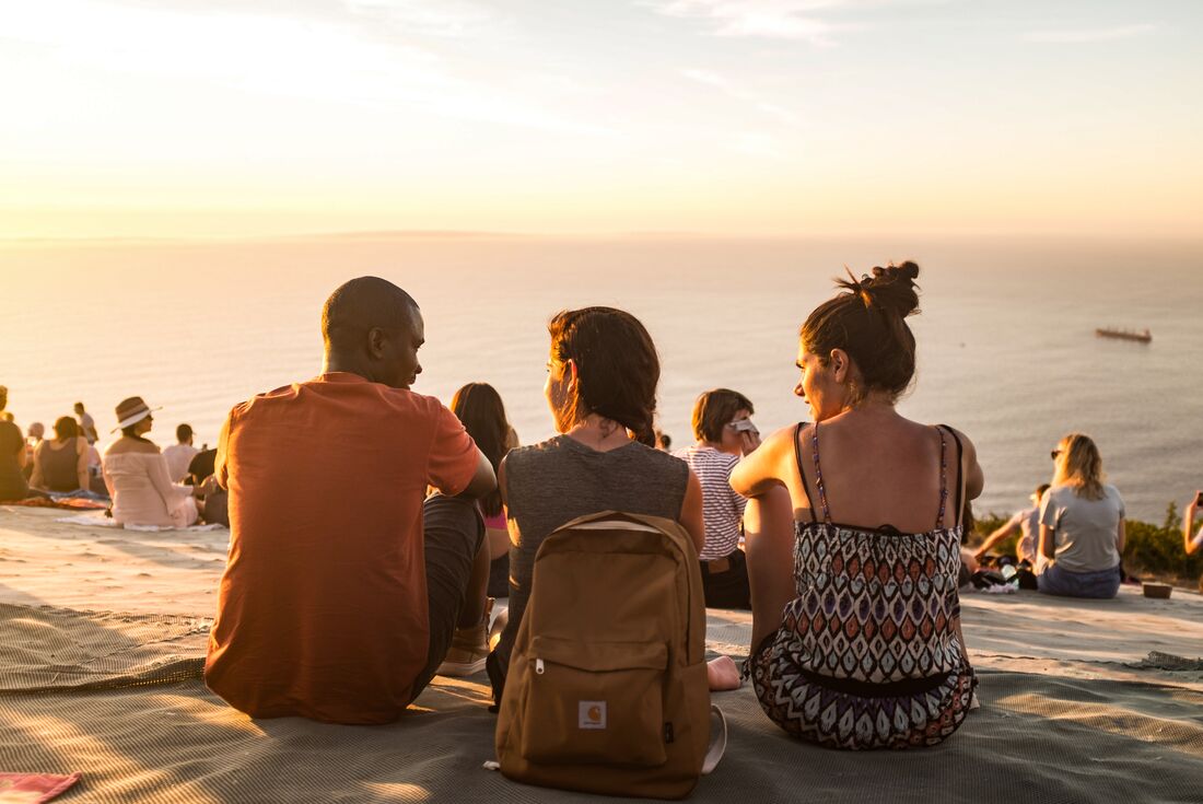 Travellers chat while sitting on the cliffs of Cape Town at sunset