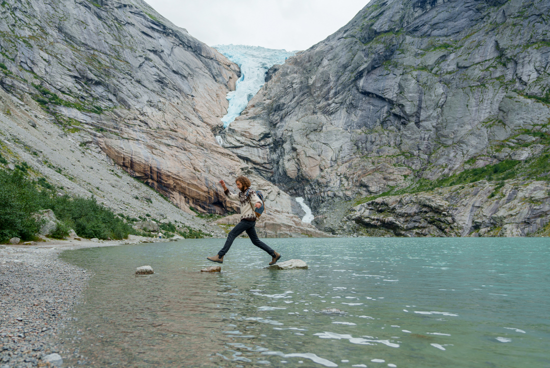 Intrepid traveller carefree rock hopping before Briksdalen Glacier, Jostedalsbreen National Park in Norway