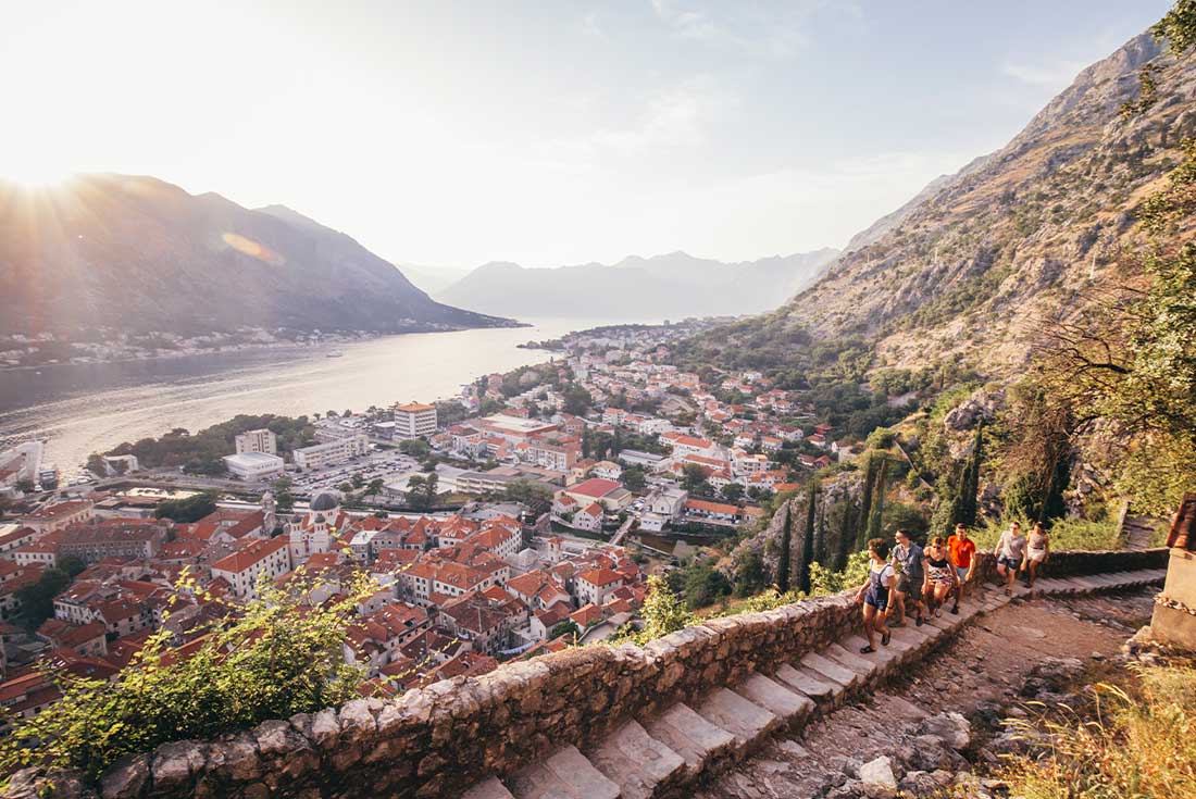 Travellers walk up steps to lookout over Koto harbour and city